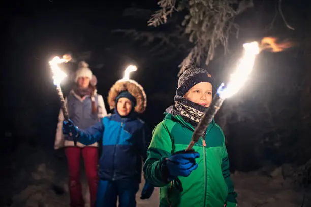 Three kids hiking in beautiful winter forest at night. Kids are holding flaming torches.
Nikon D850