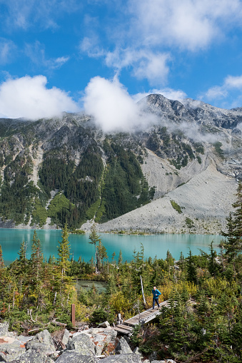 A male hiker crosses a wooden bridge near Joffre lake. Hiker has a backpack over his shoulders. Hiking in nature