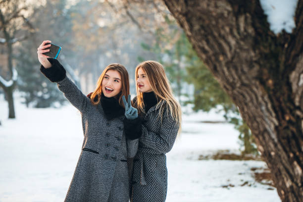 Two young Caucasian beautiful women making selfies in the snow.