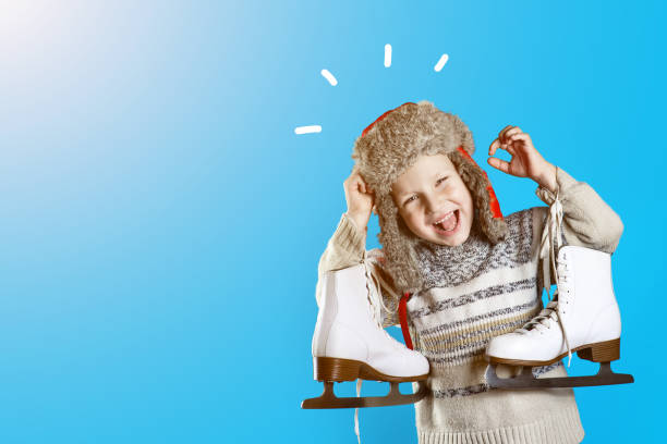cheerful boy in a hat with earflaps holding ice skates on a blue background