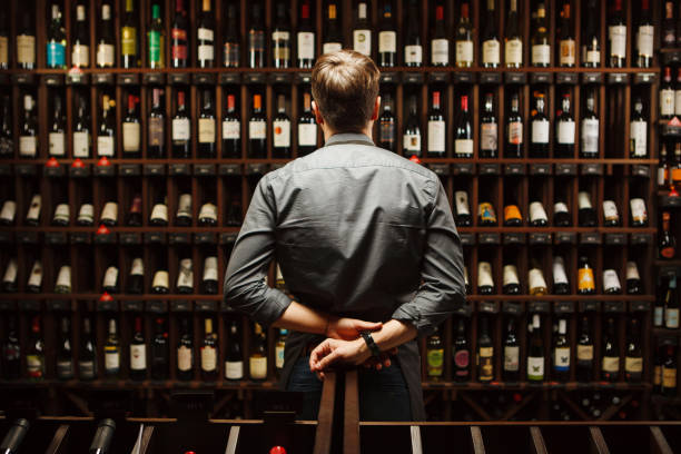 Bartender at wine cellar full of bottles with exquisite drinks Bartender at wine cellar full of bottles with exquisite alcohol drinks that have various sweet and sour tastes and dates of manufacture on large wooden shelves. wine bottle photos stock pictures, royalty-free photos & images