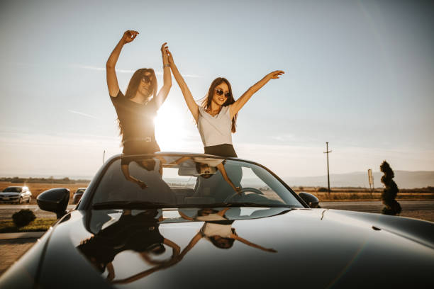 istock Girlfriends standing in cabriolet with arms raised on sunny day 1181377466