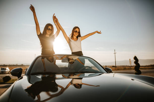 istock Happy girlfriends with raised arms in a convertible during vacation 1181378164