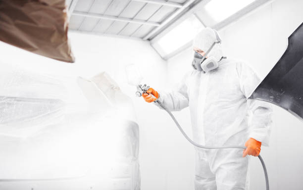 istock Worker paints auto with spray gun. White car in a paint chamber during repair work. 1181380142