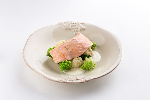 Steamed salmon, cauliflower and broccoli on white plate isolated on white background side view