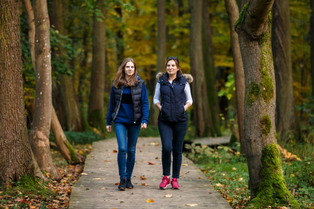 Rear-view of a young woman hiking along a narrow path through lush green woodland, with dappled sunlight and fallen leaves underfoot. Peaceful outdoor scene conveying nature, adventure, mindfulness, wellness, weekend getaway, and eco-travel themes with ample copy space.