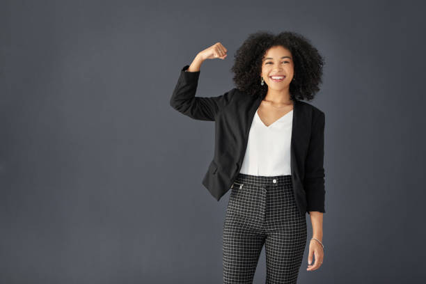 She's a powerful and influential figure in the business world Studio portrait of an attractive young corporate businesswoman flexing her bicep against a grey background flexing muscles stock pictures, royalty-free photos & images