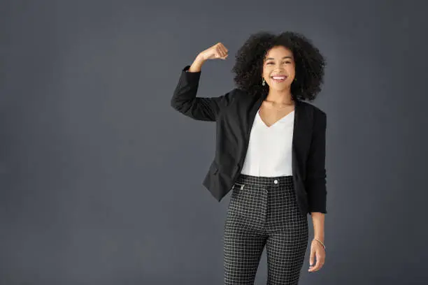 Studio portrait of an attractive young corporate businesswoman flexing her bicep against a grey background