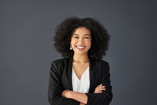 Studio portrait of an attractive young corporate businesswoman posing with her arms folded against a grey background