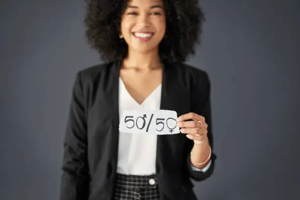 Studio shot of an unrecognizable businesswoman holding a piece of paper promoting gender equality against a grey background