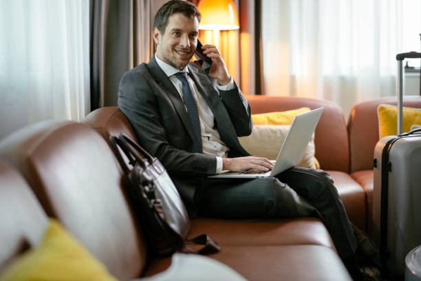 istock Businessman on sofa in hotel using laptop and phone 1181386007