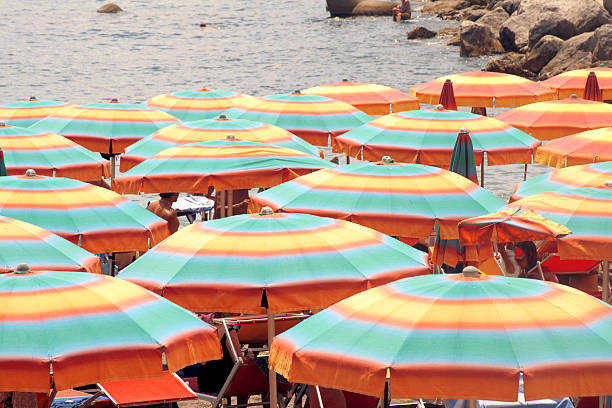 Woven white parasols arranged closely together, providing shade at beach. Detailed pattern of parasols fabric, along with fringe hanging from edges, creates an aesthetically pleasing
