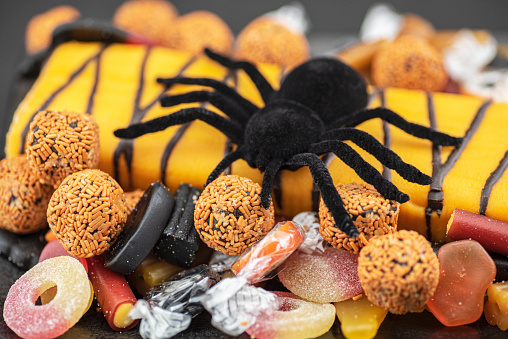 Close-up of a pumpkin roulade in a black dish decorated with candy and a black spider on top.