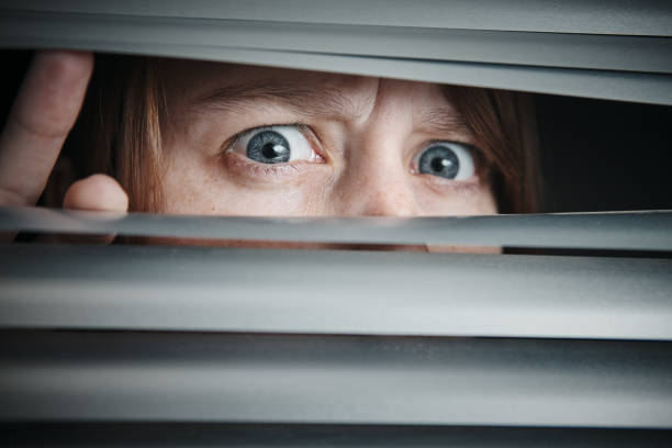 istock Frowning, frightened girl peeps through venetian blinds 1181388021