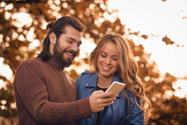 istock Young couple using cellphone in autumn colored park. 1181390824