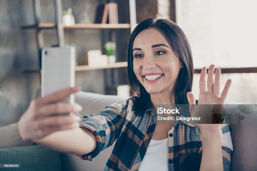 Photo of charming lady holding telephone making selfies speaking skype waving palm saying hi sitting comfort sofa wear casual checkered shirt apartment indoors - Royalty-free Filmar Foto de stock