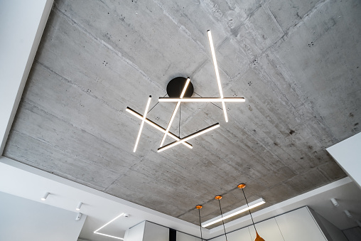 Modern ceiling LED lamp made from stripes attached to concrete ceiling. Urban interior.