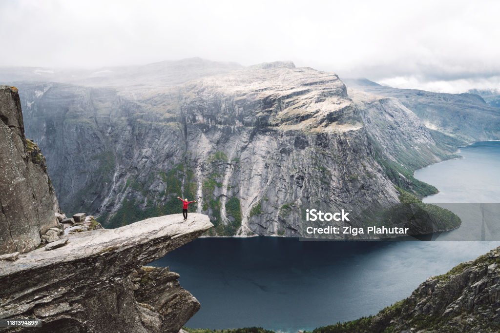 Woman standing on Trolltunga Trolltunga rock with a characteristic shape located in Norway on the border of the Hardangervidda plateau, close to the town Tyssedal. It is a popular tourist attraction in Norway and heavily visited by tourists during the summer months. Trolltunga Stock Photo