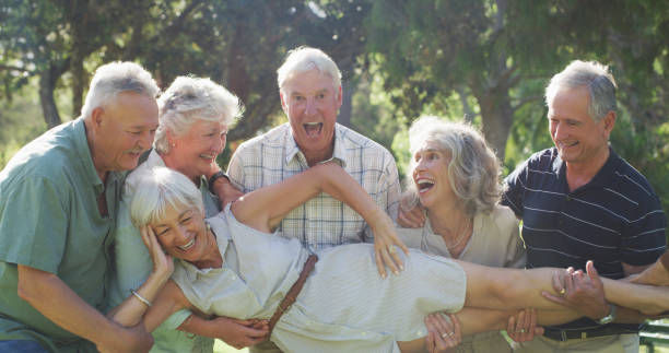 Fun is the theme of their retirement Cropped shot of a group of senior friends carrying their female friend while enjoying a day at the park 70s theme stock pictures, royalty-free photos & images
