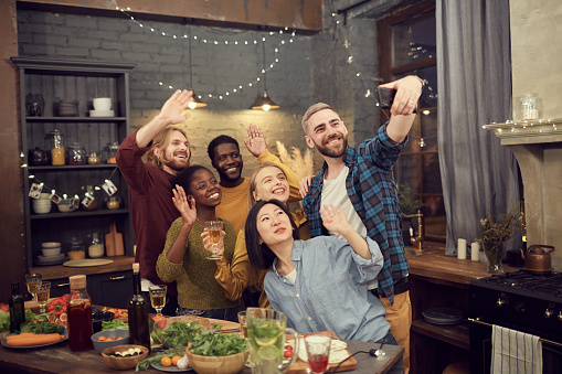 Multi-ethnic group of young people taking selfie photo via smartphone while enjoying party and dinner together