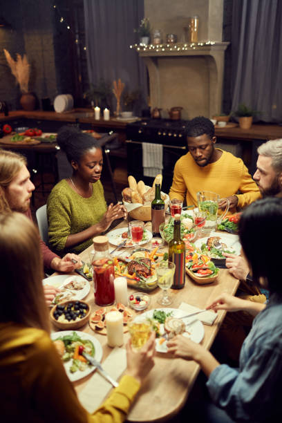 Friends Enjoying Dinner at Home High angle view at group of young people enjoying dinner and wine together sitting at table in dimly lit room, copy space big family table stock pictures, royalty-free photos & images