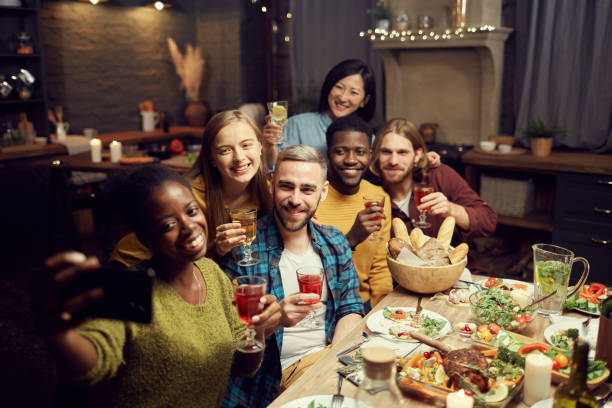 Friends Taking Selfie Photo at Dinner Party Multi-ethnic group of young people taking selfie photo via smartphone while enjoying dinner party at home, copy space big family table stock pictures, royalty-free photos & images