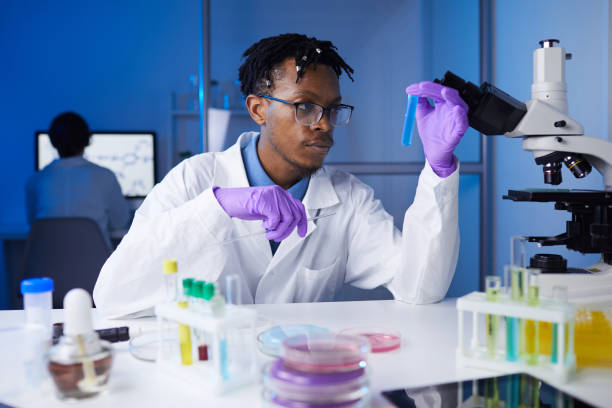 Young African Man Working in Laboratory Portrait of young African-American man holding test tube samples while working on medical research in laboratory, copy space african american scientist stock pictures, royalty-free photos & images