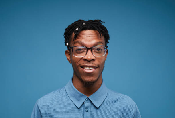 Contemporary African Man Smiling on Blue Head and shoulders portrait of young African-American man smiling at camera while posing against blue background, copy space black nerd stock pictures, royalty-free photos & images