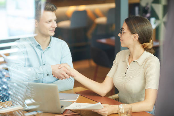 istock Content satisfied young business people sitting at table in restaurant and making handshake while congratulating each other with successful project 1181402198