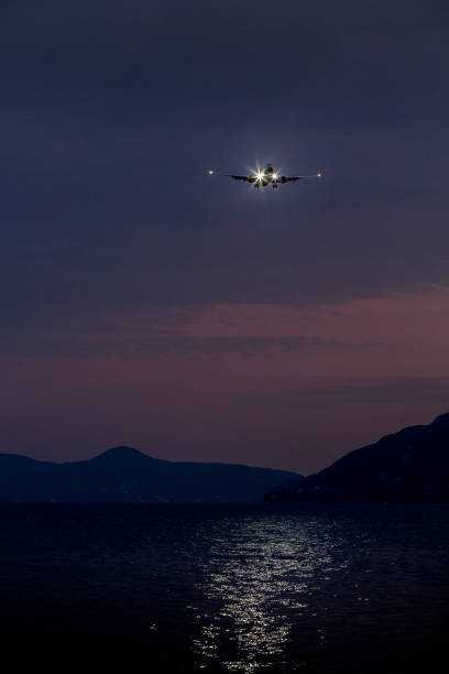 istock Jet aircraft on landing approach flying low over water by night 1181402359