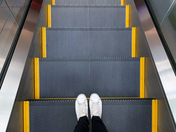 Selfie dos pés nas sapatas brancas das sapatilhas que estão na escada rolante na Alameda de compra ou no escritório moderno - foto de acervo