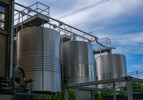 Stainless tanks for processing and fermentation and processing of grapes. Wine production in Spain, Catalunya. Steel tanks in the open air with wine on blue sky background. Modern wine factory.