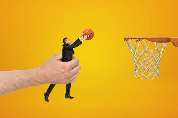 большой мужчина стороны проведения бизнесмен с баскетбольным мячом протягивая руку обруч на желтом фоне - basketball sport human hand reaching стоковые фото и изображения