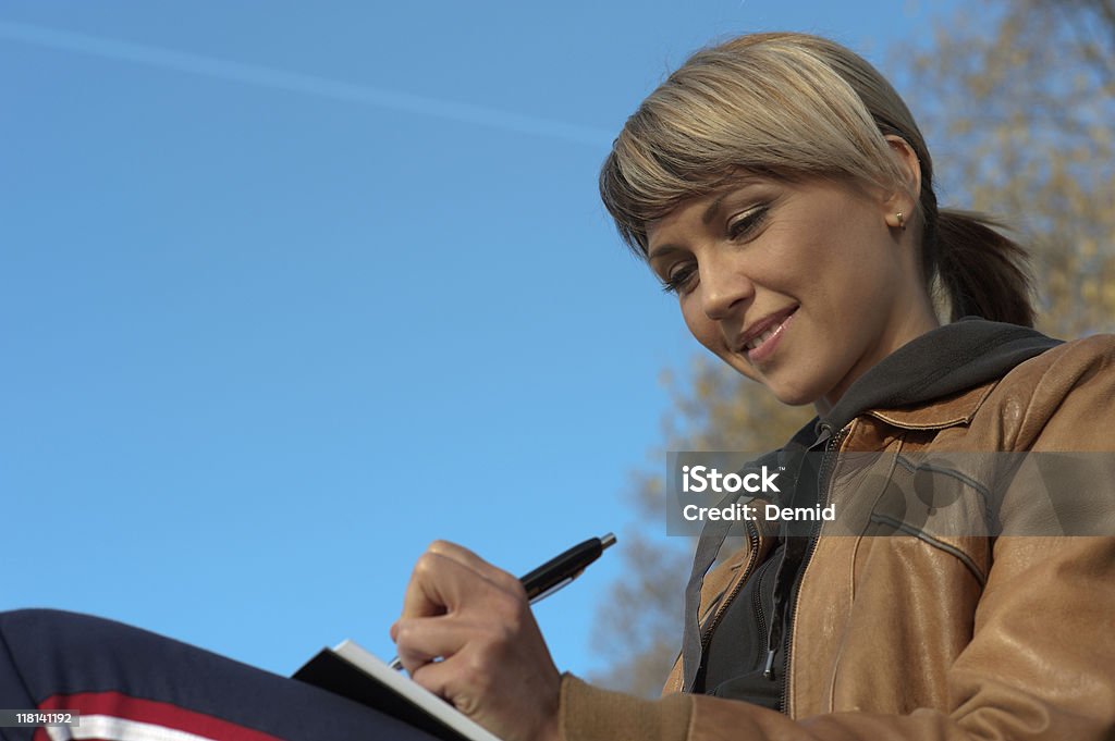 Lady Writing Outdoors Woman writing in a park, sky on the background. Activity Stock Photo