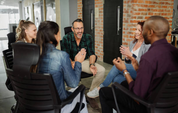 un gruppo eterogeneo di uomini d'affari seduti in cerchio. bell'uomo che parla con i colleghi in una sessione di team building. - abbigliamento casual foto e immagini stock