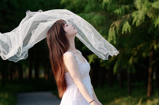 Portrait of beautiful Chinese girl in white wedding dress raise her head waiting fly wedding veil to cover her face.