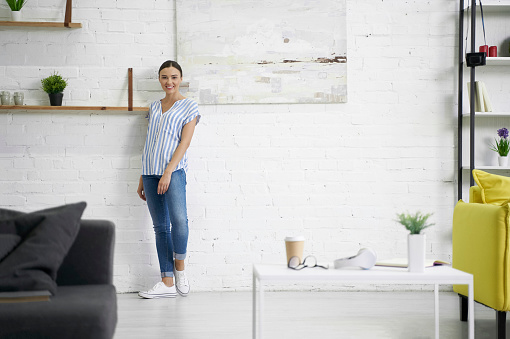 Confident positive young woman standing by the white wall next to the picture