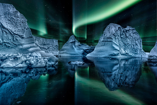 iceberg floating in greenland fjord at night with green northern lights