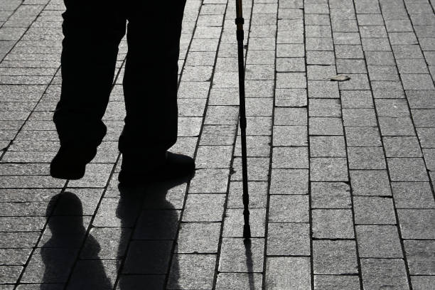 istock Silhouette of limping man walking with a cane, long shadow on pavement 1181436522