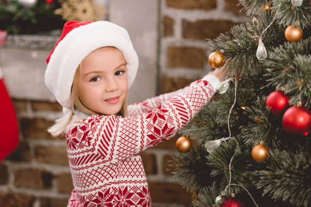 istock cute kid in santa hat and sweater decorating christmas tree 1181438548