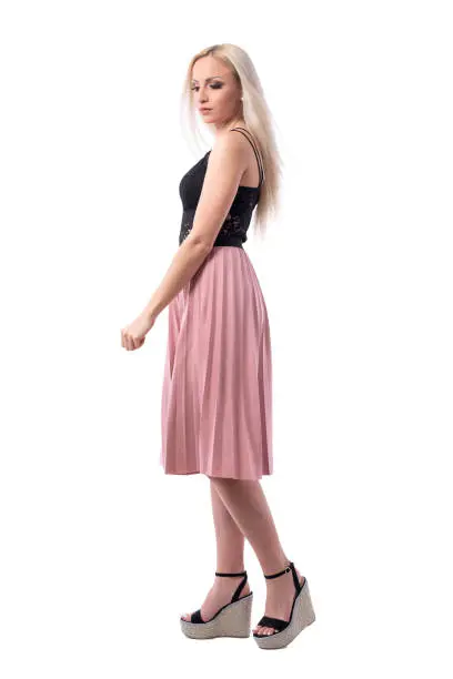 Glamour feminine blonde young woman in pink pleated skirt walking and looking down. Full body isolated on white background.