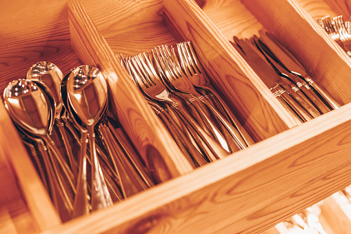 Spoons, forks, knives in the tray. Wooden drawer with modern cutlery. Kitchen or restaurant concept background