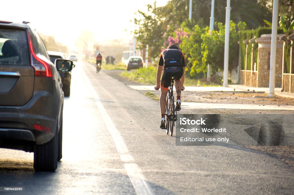 Ciclista montar en bicicleta en la carretera a lo largo de los coches que pasan a su lado y mantener la distancia de seguridad con bicicletas. - Foto de stock de Andar en bicicleta libre de derechos