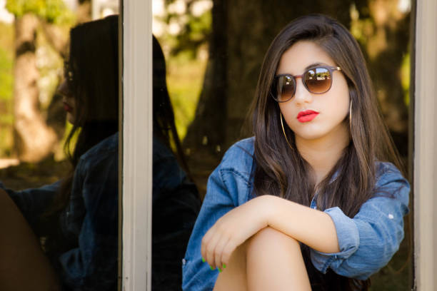 teen girl sitting in front of wide door with mirrors reflecting the nature of the park