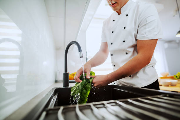 istock Cropped image of dedicated caucasian chef washing spinach in kitchen sink. Kitchen interior. 1181450624
