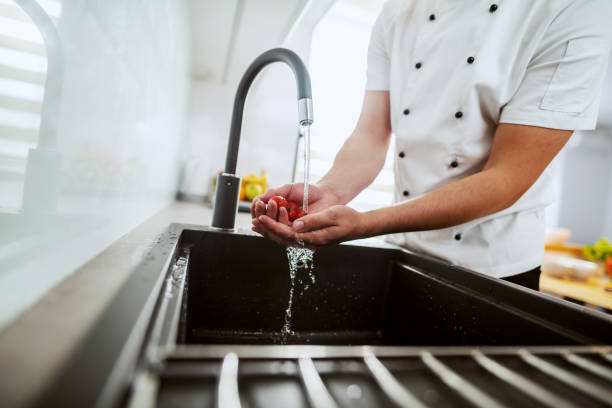 istock Cropped image of dedicated caucasian chef washing cherry tomato in kitchen sink. Kitchen interior. 1181450663