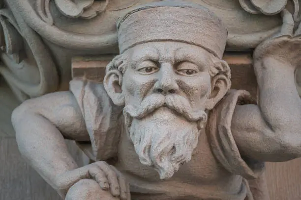 Photo of Sculpture of an old small and bearded funny man, dwarf, as an atlant in downtown of Magdeburg, Germany, closeup, details