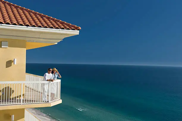 Young man and woman standing on the balcony looking out over the beautiful blue ocean.