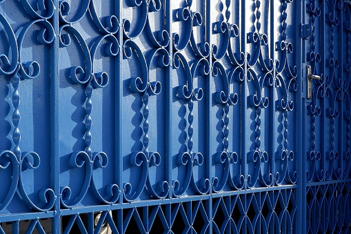 Sunlight and shadow on surface of wrought-iron elements pattern of vintage blue metal gate door decoration, exterior architecture concept
