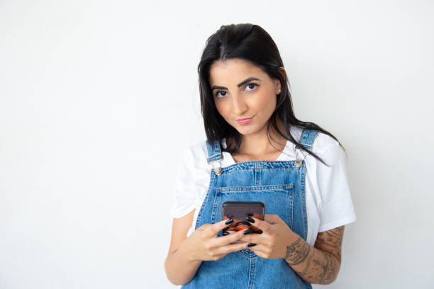 istock Charming smiling girl holding phone while looking at camera 1181455968